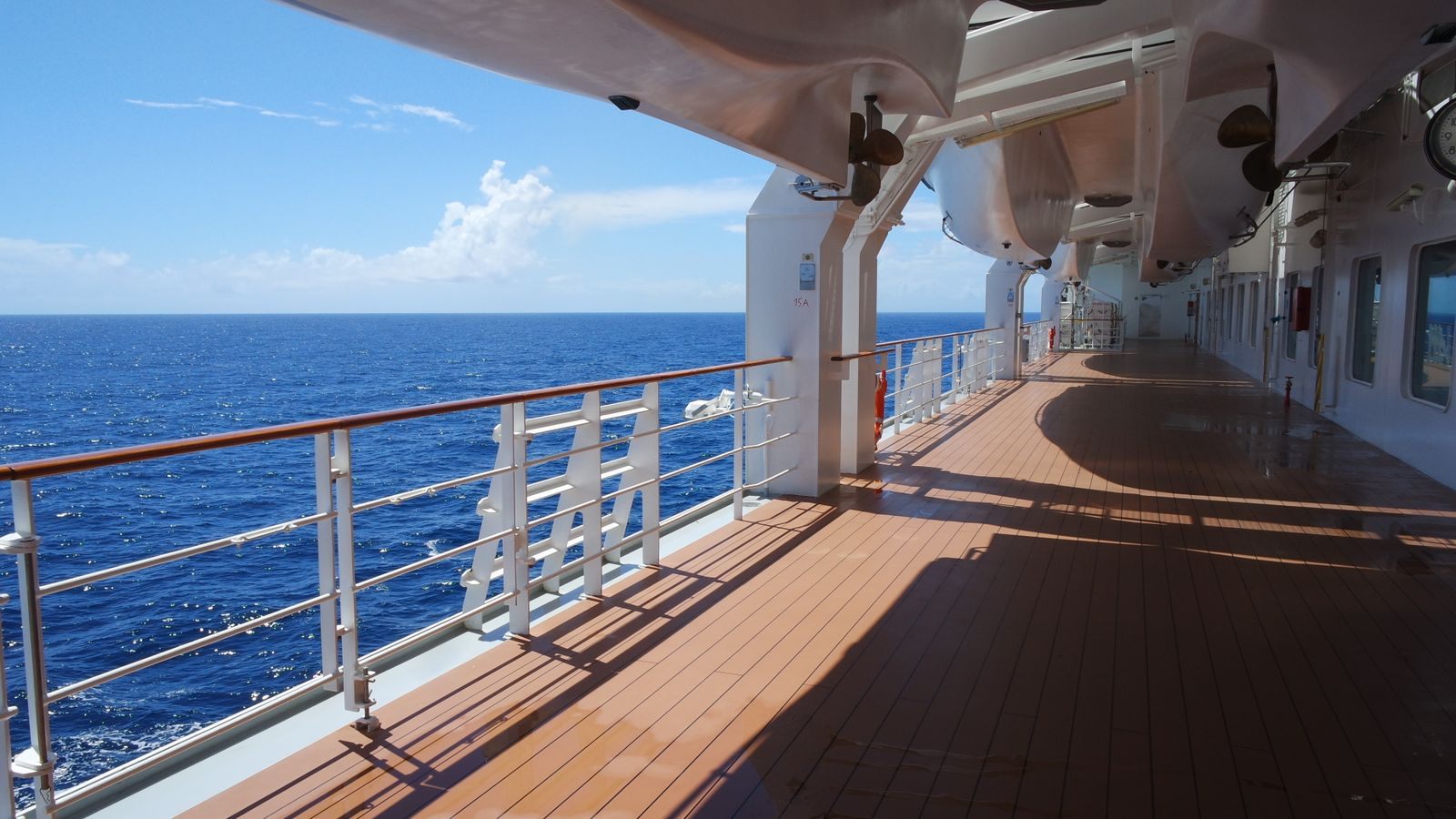 Sunny teak promenade deck and railing of a cruise ship above a deep blue sea, the best cruise for a senior trip has room to gather