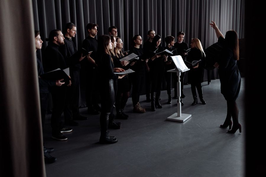 Choir dressed in black rehearsing with a conductor and music stand