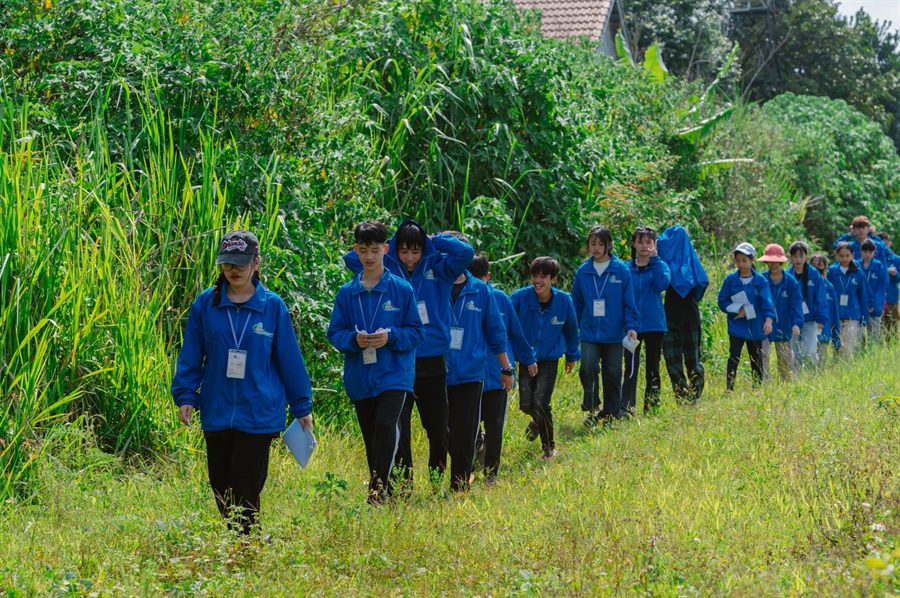 Line of students in matching blue jackets walking a grassy trail with a leader