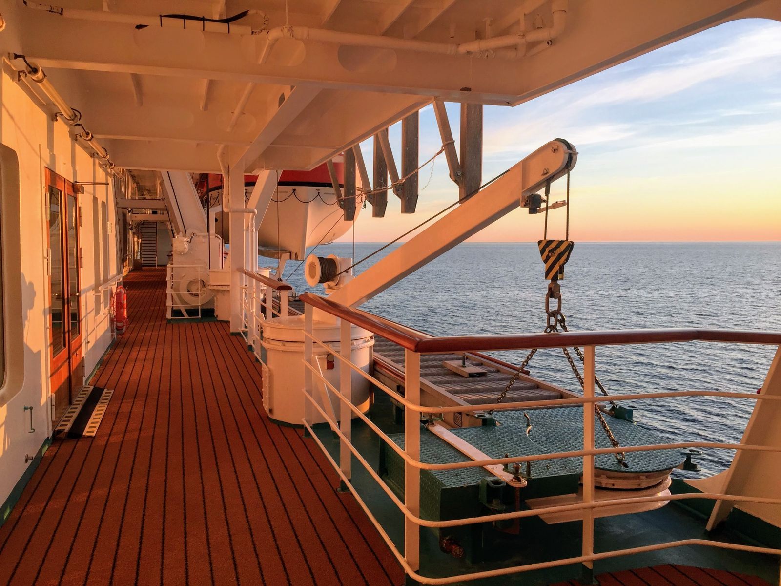 Quiet promenade deck of a ship with lifeboat davits at sunset, the kind of sailing senior trip packages are built around