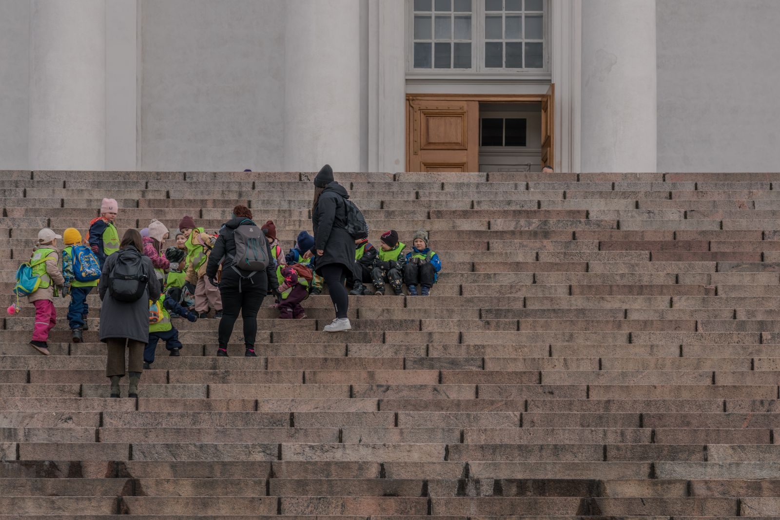 Teachers and children with backpacks on the wide stone steps of a building during a school trip