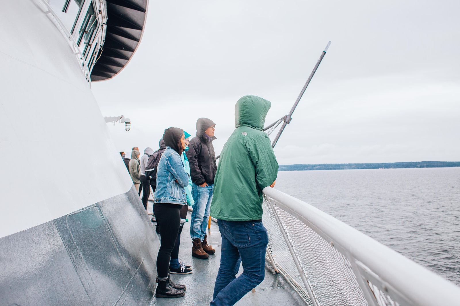 Passengers in rain jackets watching the sea from the rail of a ship